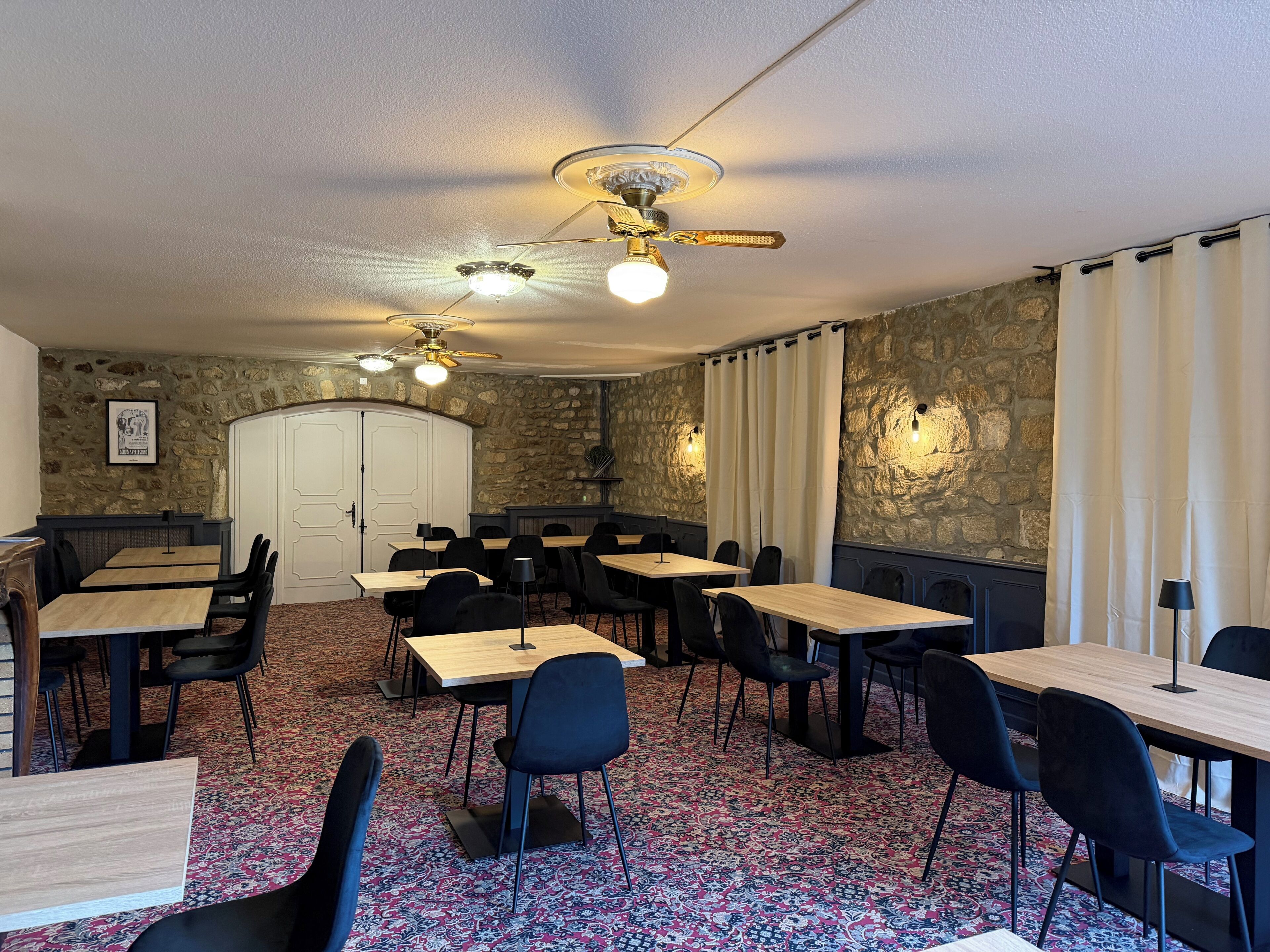 Une salle de conférence équipée de tables, de chaises, d’un ventilateur de plafond et de murs en pierre.