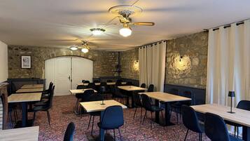 Une salle de conférence équipée de tables, de chaises, d’un ventilateur de plafond et de murs en pierre.