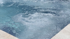 A swimming pool with water jets, a sun umbrella, and lounge chairs. - Le moulin de barette (Blavozy)
