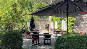 An outdoor patio with tables and chairs, surrounded by greenery and stone walls. - Le moulin de barette (Blavozy)