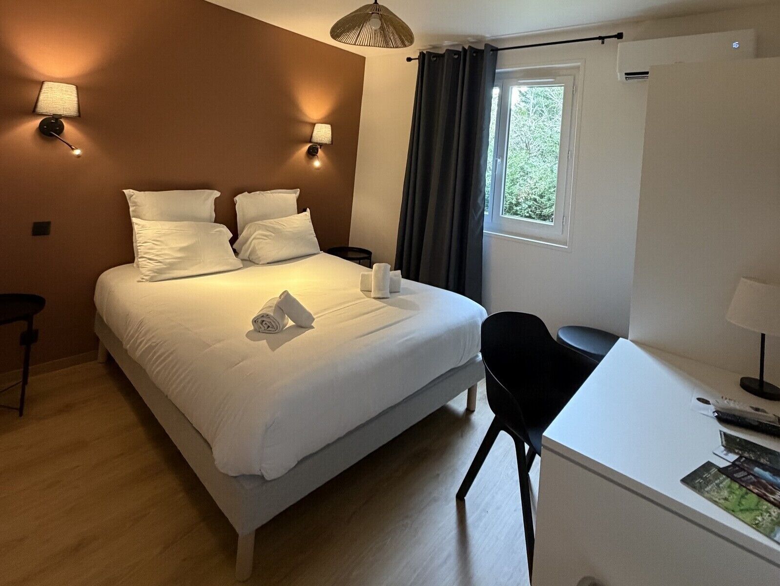 Een hotelkamer met een bed, nachtkastjes, een bureau en een raam met gordijnen.