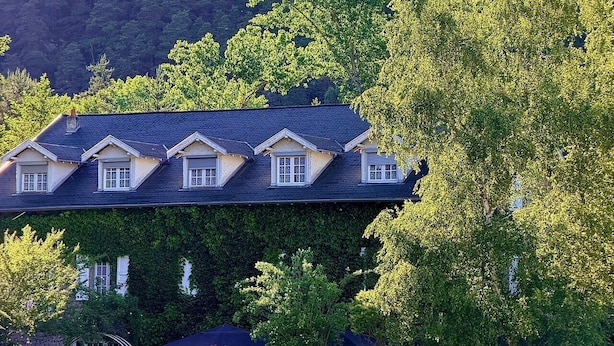 A building with a dark roof, multiple windows, and a parking sign. - Le moulin de barette (Blavozy)