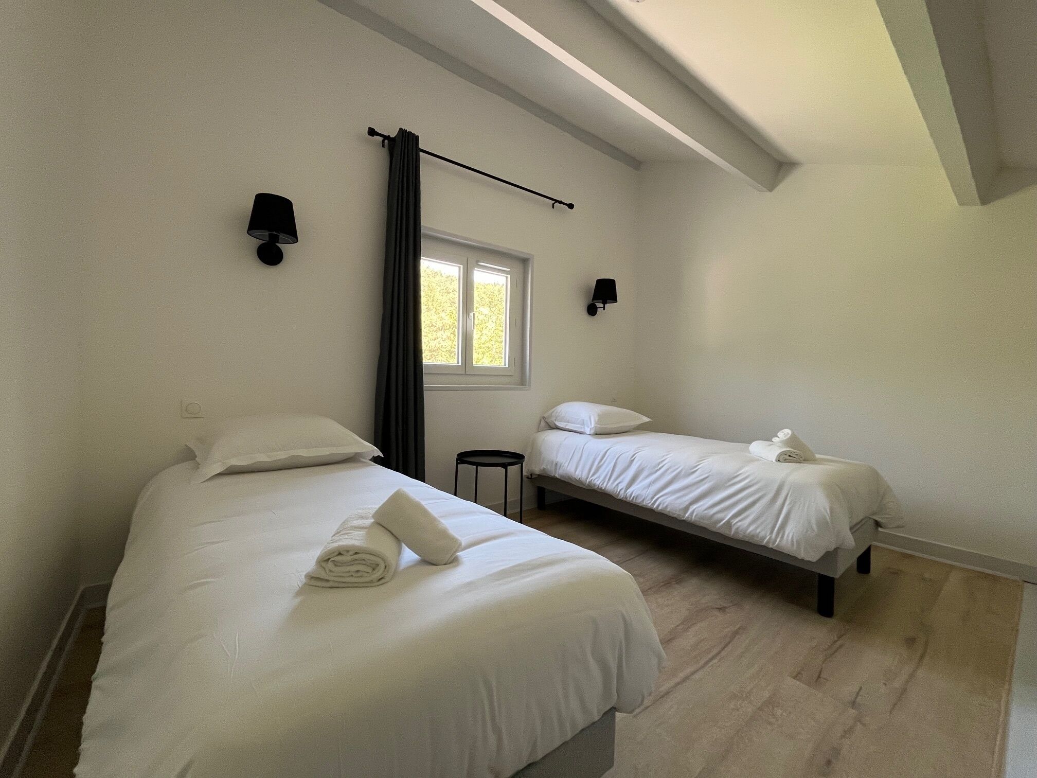 A bedroom with two beds, a window, and a curtain.