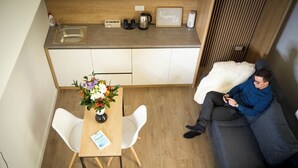 A compact living space with a kitchenette, a dining area with a table and chairs, and a sofa with a person sitting on it. - FRIENDS RESIDENCE (Timisoara)