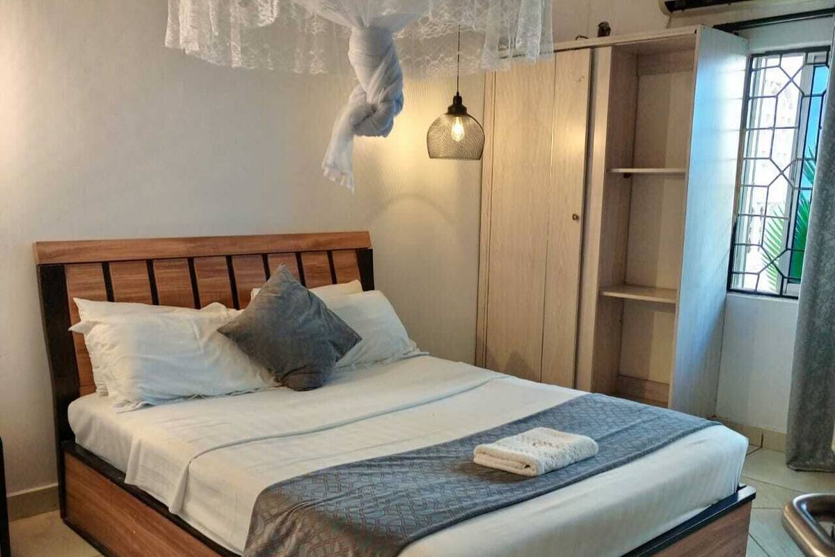A neatly made bed with a wooden headboard, a bedside lamp, and a window with a view of greenery.