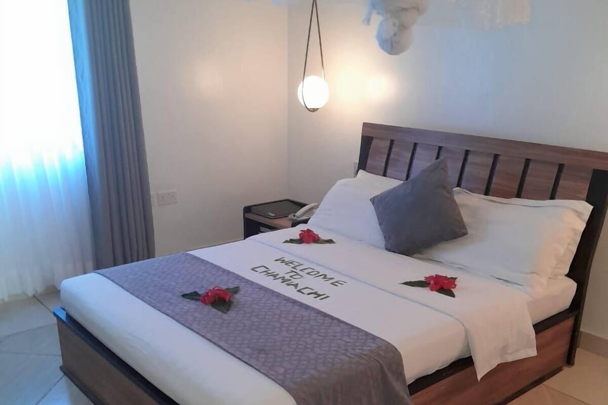 A neatly made bed with a welcome mat, pillows, and a bedside table with a lamp.