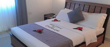 A neatly made bed with a welcome mat, pillows, and a bedside table with a lamp.