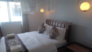 A neatly made bed with a wooden headboard, two patterned pillows, and a white bedspread. There is a small wooden nightstand beside the bed.