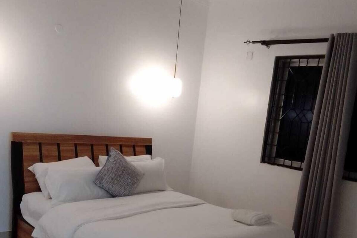 A neatly made bed with a wooden headboard, a bedside lamp, and a window with curtains.