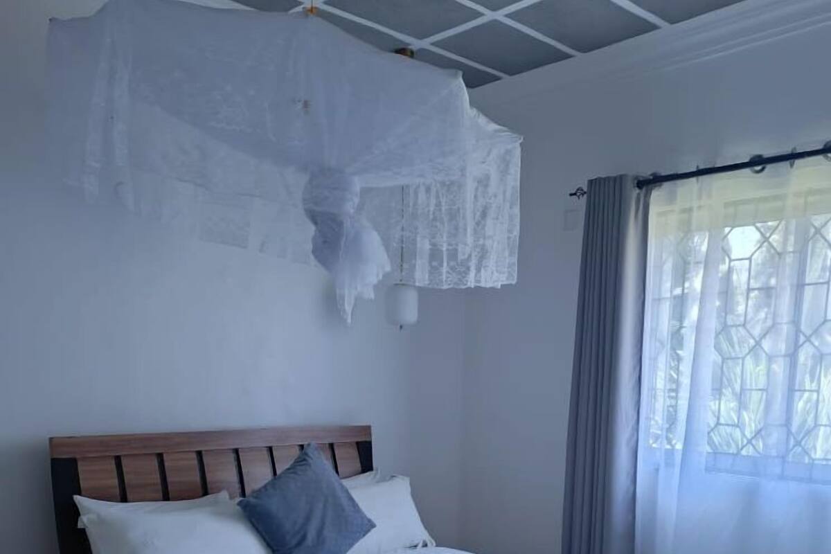 A neatly made bed with a wooden headboard, a bedside table, and a window with curtains.