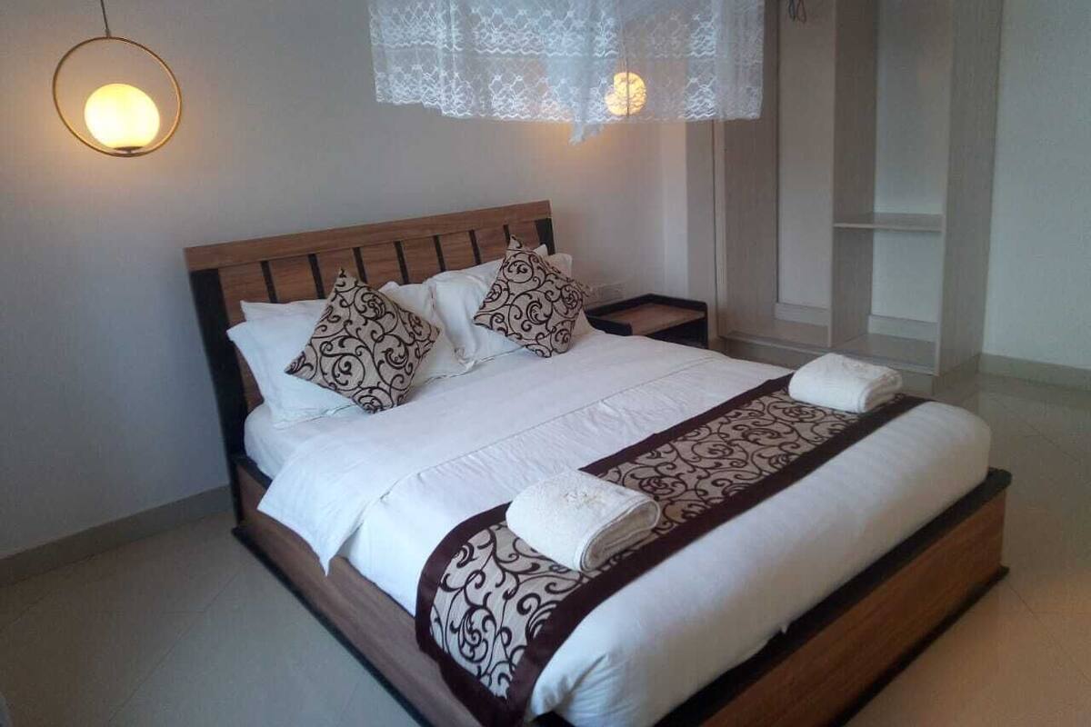 A neatly made bed with patterned pillows and a decorative throw, a bedside lamp, and a hanging lace canopy.