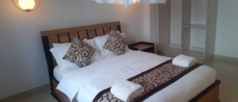 A neatly made bed with patterned pillows and a decorative throw, a bedside lamp, and a hanging lace canopy.