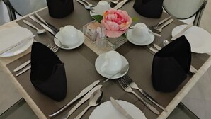 A dining table set with white plates, silverware, and black napkins. A pink flower is placed in the center. - Chamiachi Hotel and Luxury Apartments  (Mombasa)
