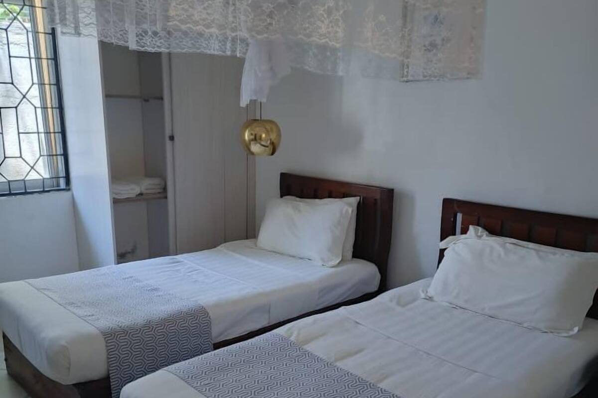Two single beds with wooden frames and white bedding, a lace canopy, and a small golden object on the wall.