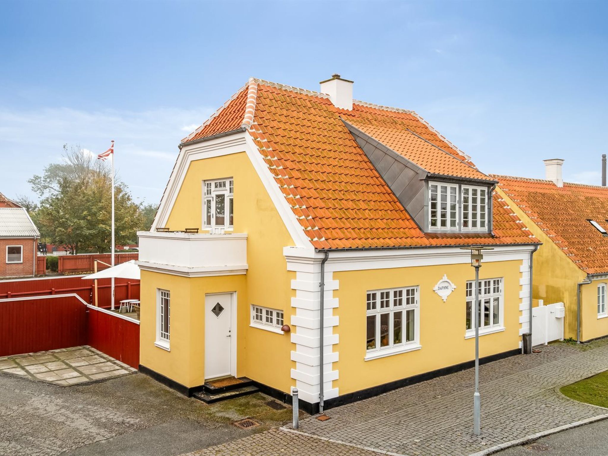 A yellow building with a red-tiled roof, white trim, and a small porch.