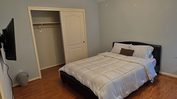 A bedroom with a bed, a closed door, a television mounted on the wall, and a trash can.