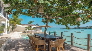 A wooden deck with a pool, wicker chairs, and a view of the sea with boats. - La Villa Ceningan by K-Club (Ceningan Island)