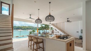 A modern kitchen with a central island, bar stools, and a view of the sea. - La Villa Ceningan by K-Club (Ceningan Island)