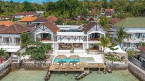 A beachfront property with a pool, lounge chairs, and a dining area. - La Villa Ceningan by K-Club (Ceningan Island)