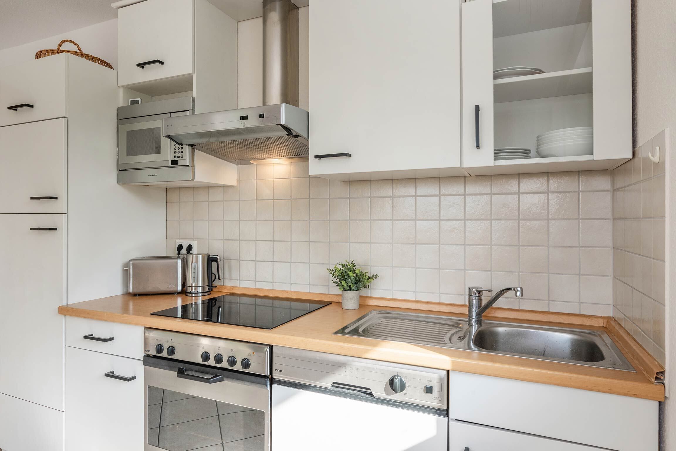 A modern kitchen with white cabinets, a stainless steel range hood, a built-in oven, a dishwasher, a double sink, and a wooden countertop.
