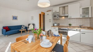 Una cocina moderna con armarios blancos, una mesa de comedor de madera y un sofá azul en la sala de estar.