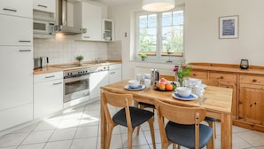 Una cocina moderna con armarios blancos, una mesa de comedor de madera y un ventanal grande.