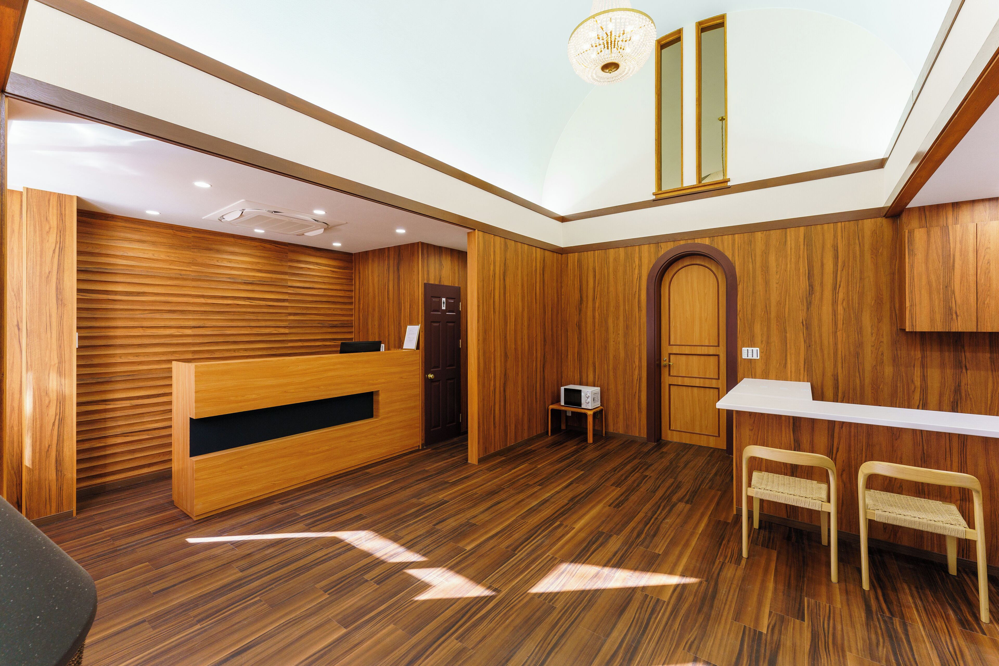 Un área de recepción con un mostrador de madera, una mesita, dos bancos y una puerta.