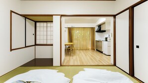 Una habitación japonesa tradicional con suelo de tatami, futón, puertas correderas y vistas a una zona de cocina.