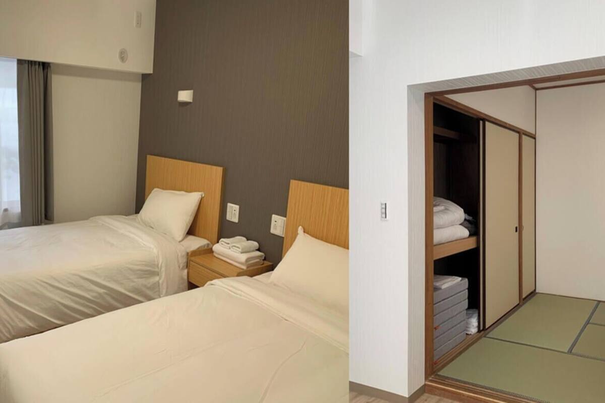 A hotel room with two beds, a wooden headboard, a bedside table with a lamp, and a wardrobe with a sliding door.