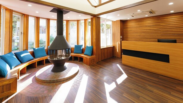Un interior moderno con chimenea central, bancos de madera con cojines azules y ventanas grandes que dejan entrar luz natural.