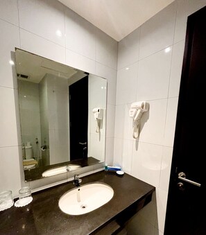 Une salle de bain équipée d’un grand miroir, d’un lavabo, d’un sèche-cheveux et d’un distributeur de serviettes.