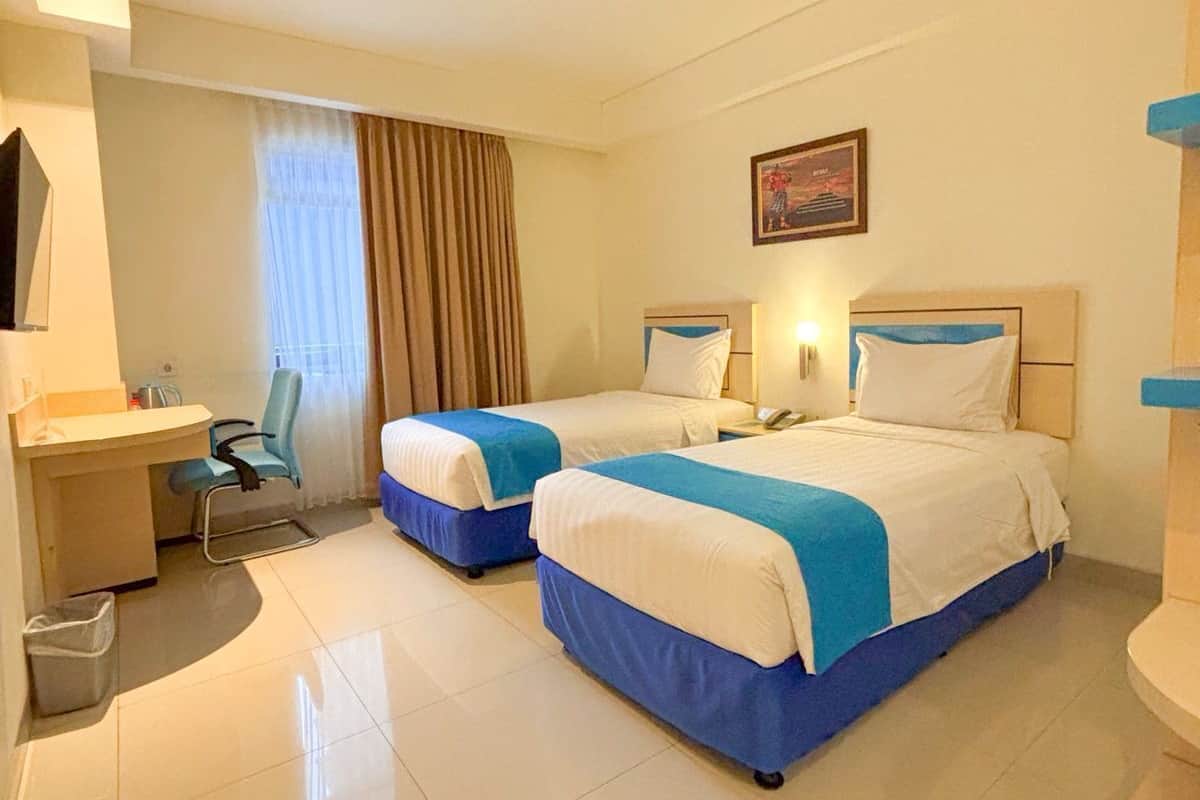 A hotel room with two beds, a desk, a chair, and a bathroom.
