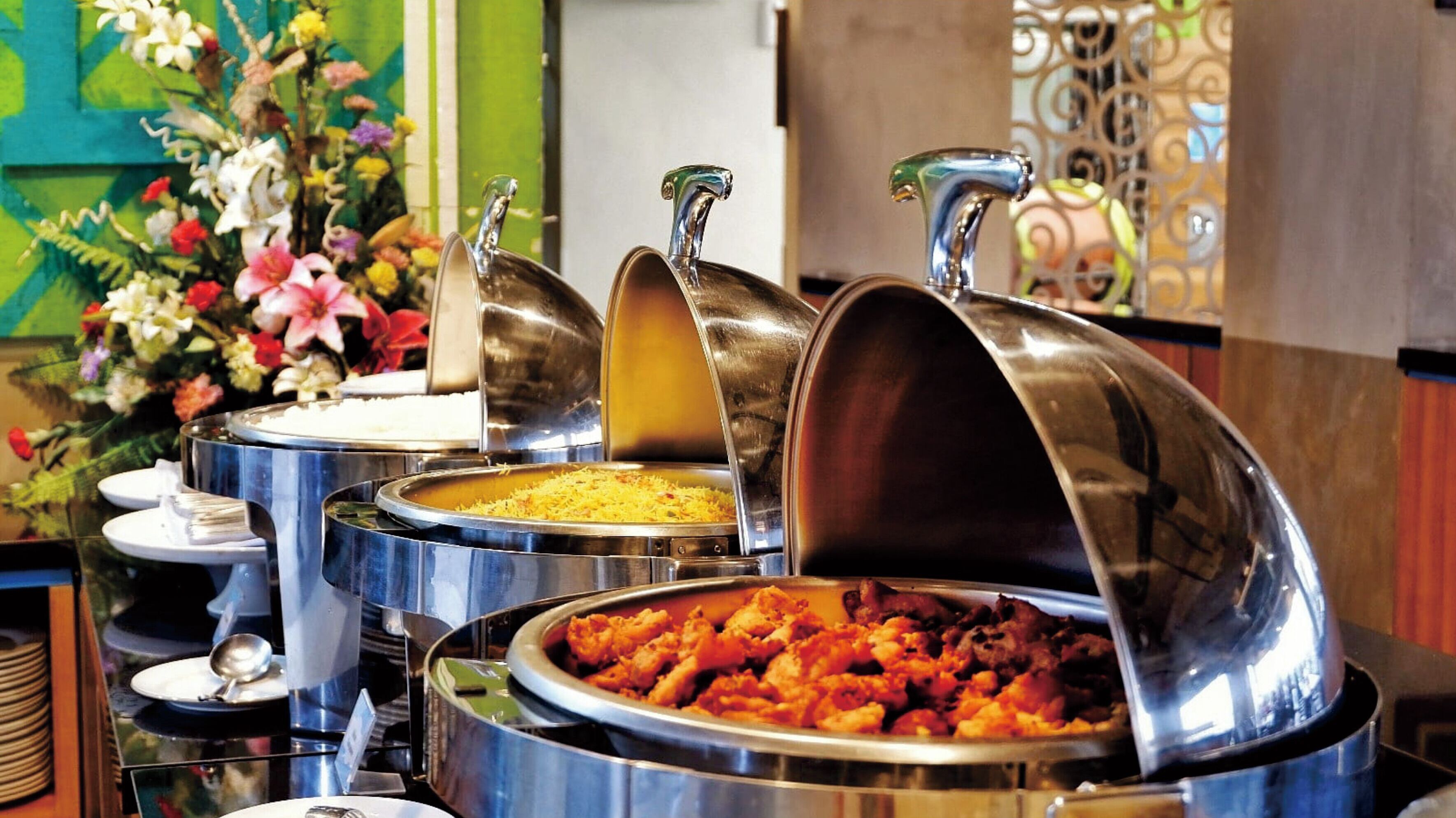 Buffet com vários rechauds de aço inoxidável contendo diversos pratos.