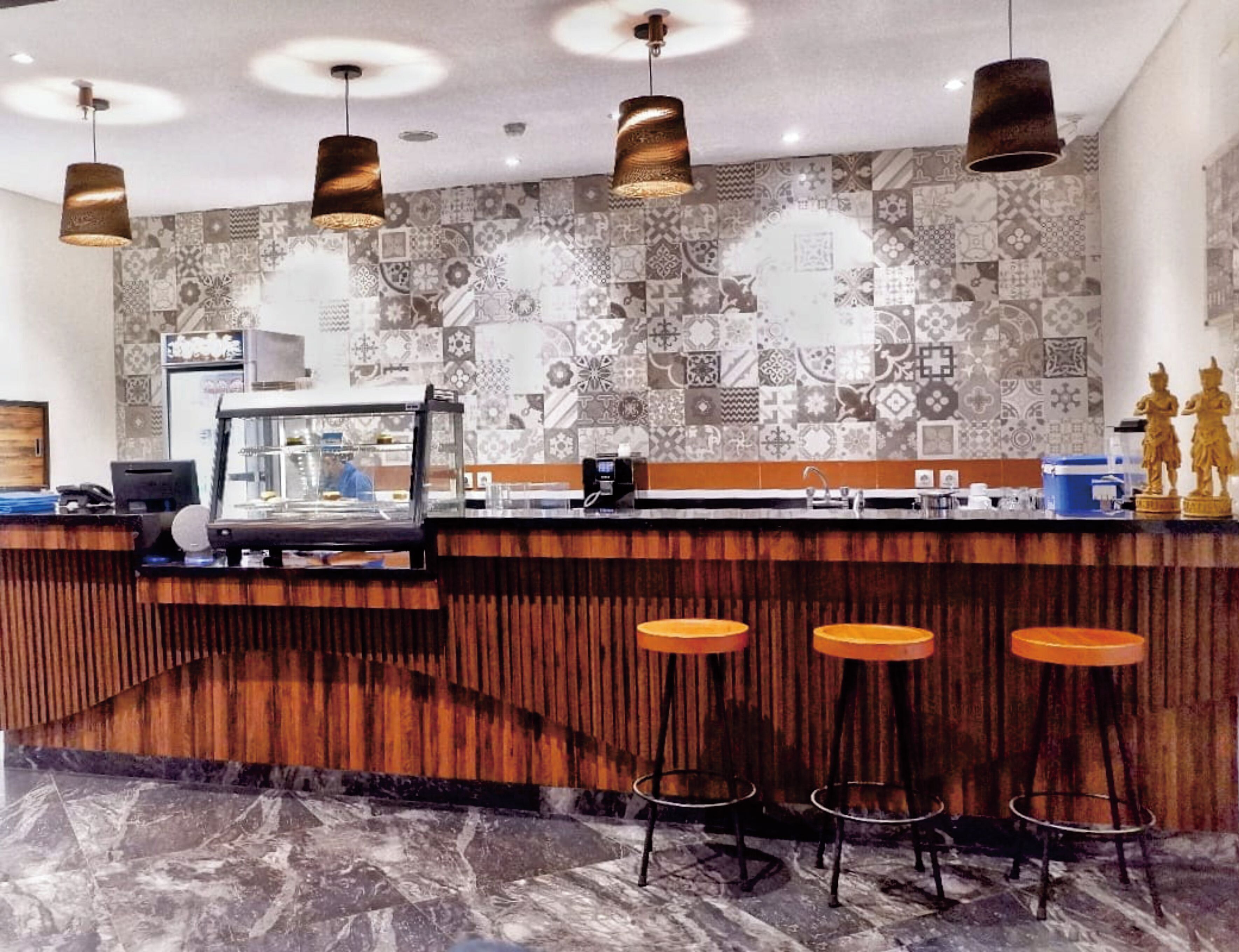A bar area with a patterned tile backsplash, wooden bar counter, and three stools.