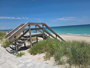 A wooden structure with a staircase leading to a beach area, surrounded by sand and vegetation.