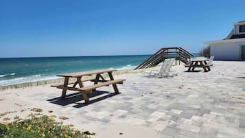 A beachside patio with picnic tables, a wooden deck, and a view of the ocean.