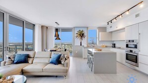 A modern apartment with a living area, kitchen, and large windows offering a city view. - 3BR Apartment with Views and Complementary Parking (Hollywood)