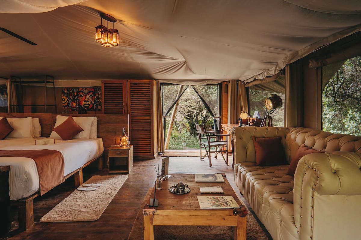 A tented accommodation with a bed, sofa, and desk area.