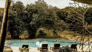 Uma piscina com espreguiçadeiras, rodeada por árvores e uma estrutura de madeira.