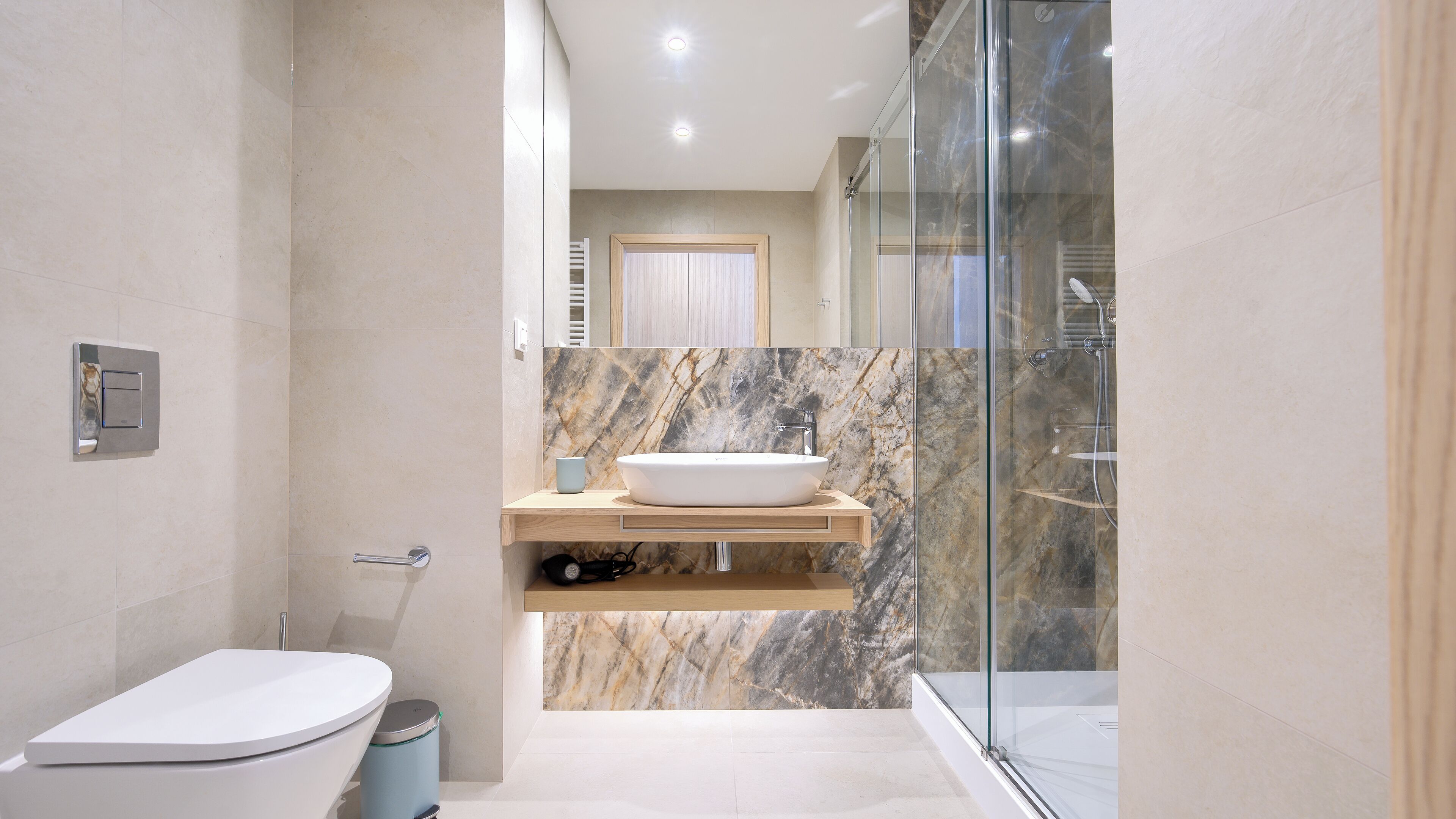 Un baño moderno con salpicadero de mármol, inodoro independiente, ducha con mampara de vidrio y tocador con lavamanos.