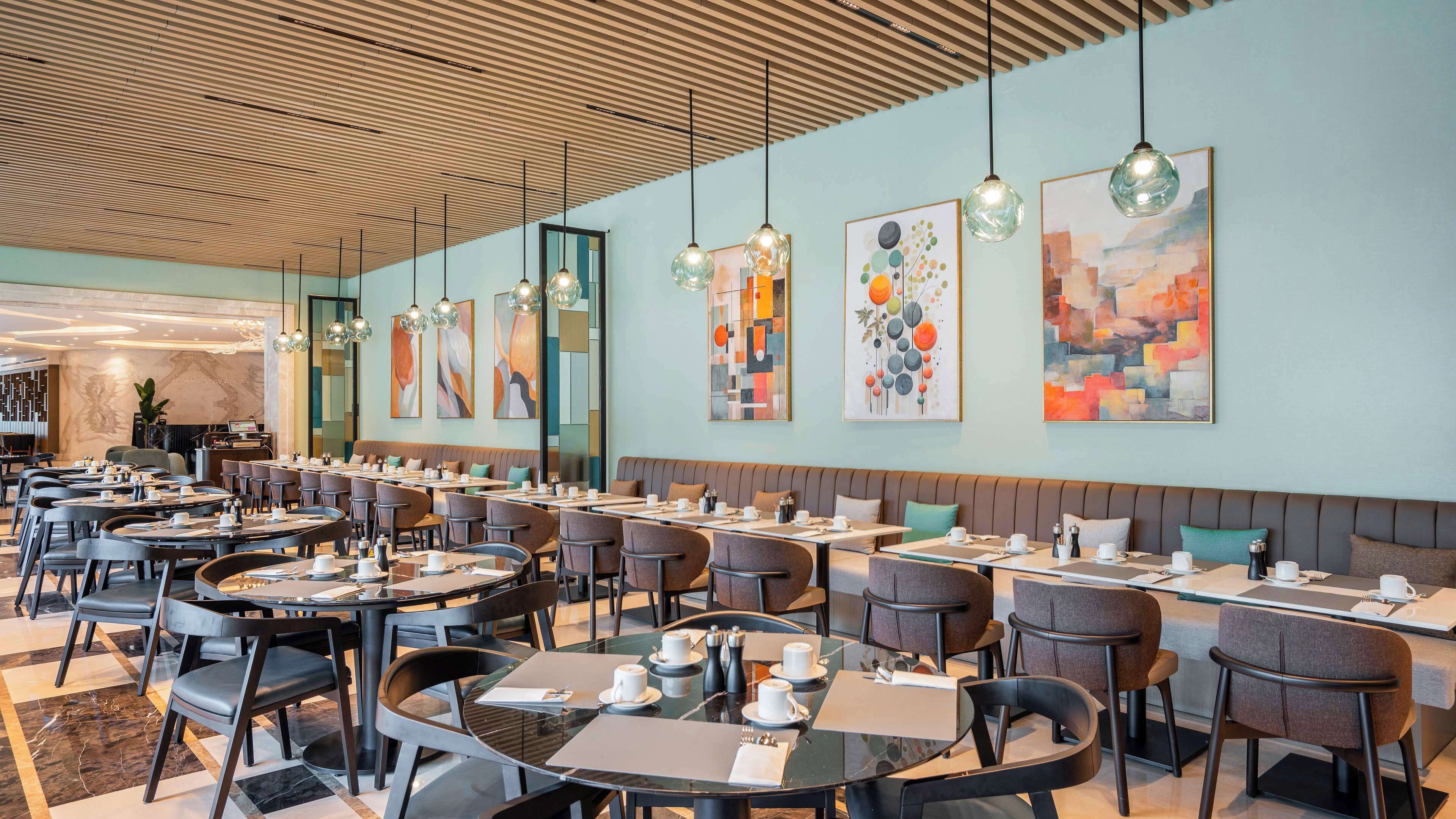 Un restaurante moderno con mesas redondas y cabinas, que presenta obras de arte contemporáneas en las paredes e iluminación colgante.
