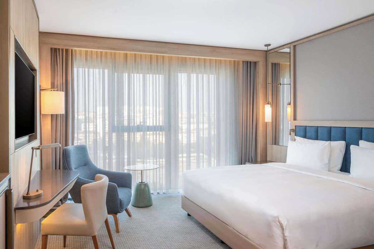 Ein Hotelzimmer mit Bett, Schreibtisch mit Stuhl, Fernseher und kleinem Tisch mit Lampe.