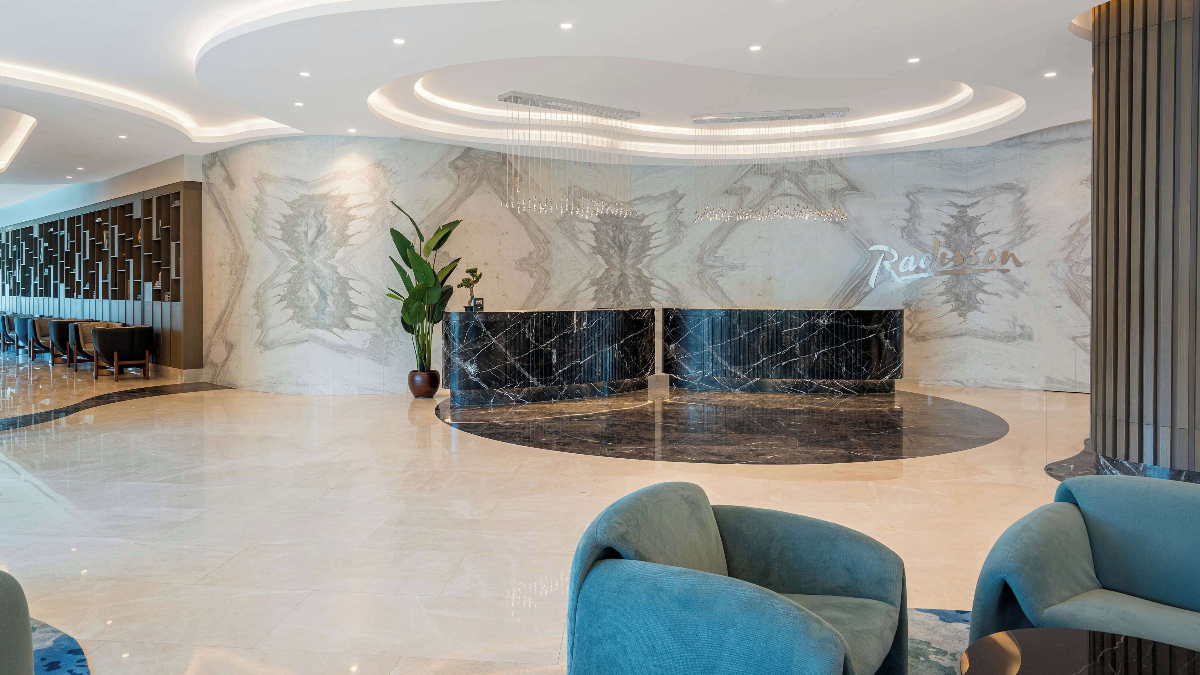 A modern lobby with a marble reception desk, seating area, and a large plant.