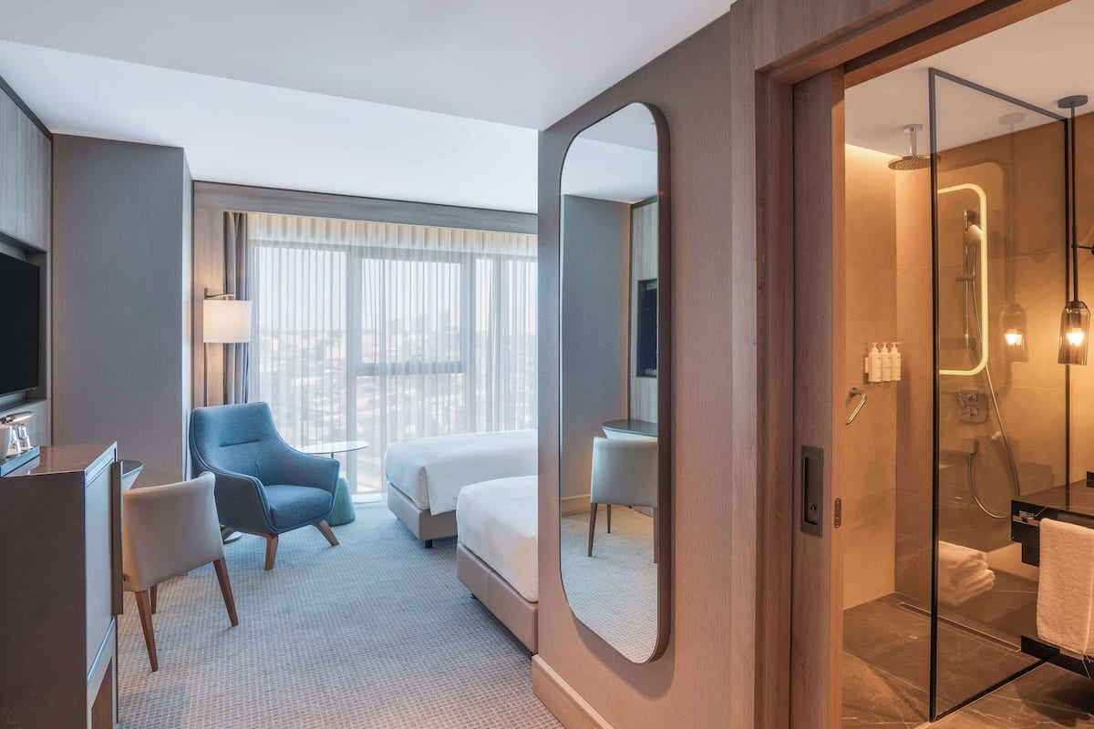 Ein modernes Hotelzimmer mit einem Bett, einem Schreibtisch, einem Sessel und einem großen Spiegel, inklusive einem Badezimmer mit Duschkabine.