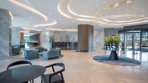 Un hall d’entrée moderne avec un comptoir de réception en marbre, un espace salon et un grand lustre.