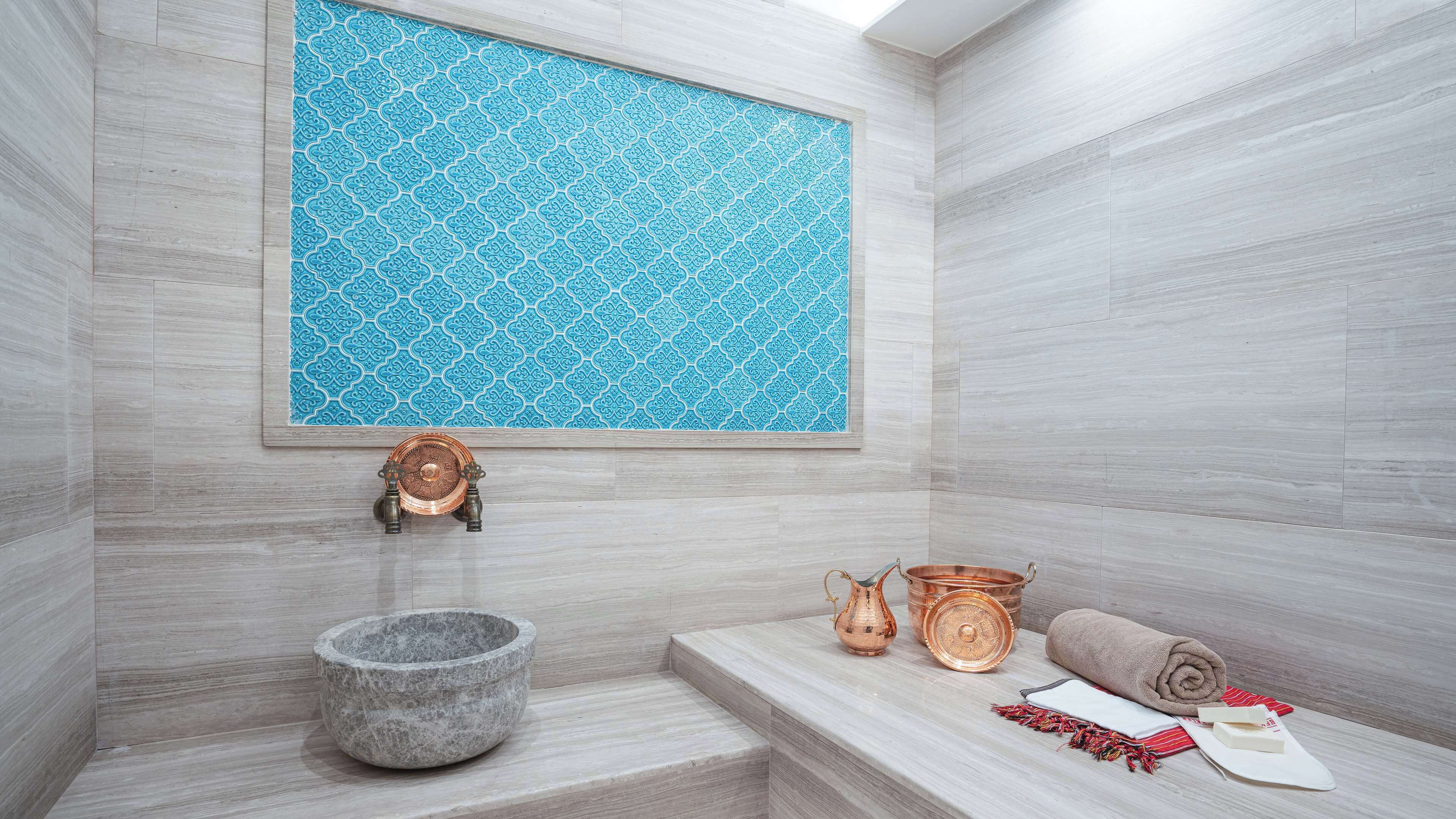 Un baño moderno con un lavabo de piedra, un recipiente de cobre y una toalla en un estante.