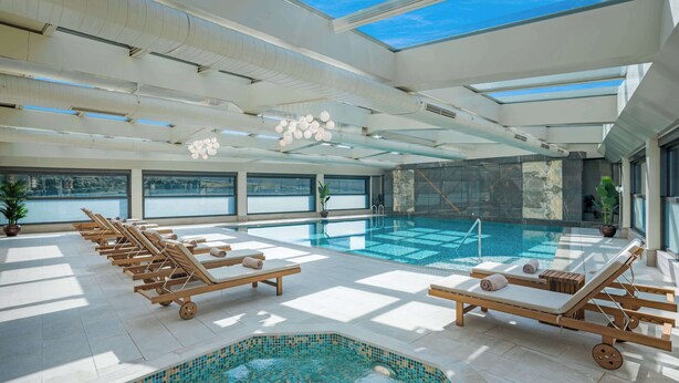 Un espace piscine intérieur moderne, doté de chaises longues, d’un petit jacuzzi et de grandes fenêtres offrant une vue sur l’extérieur.