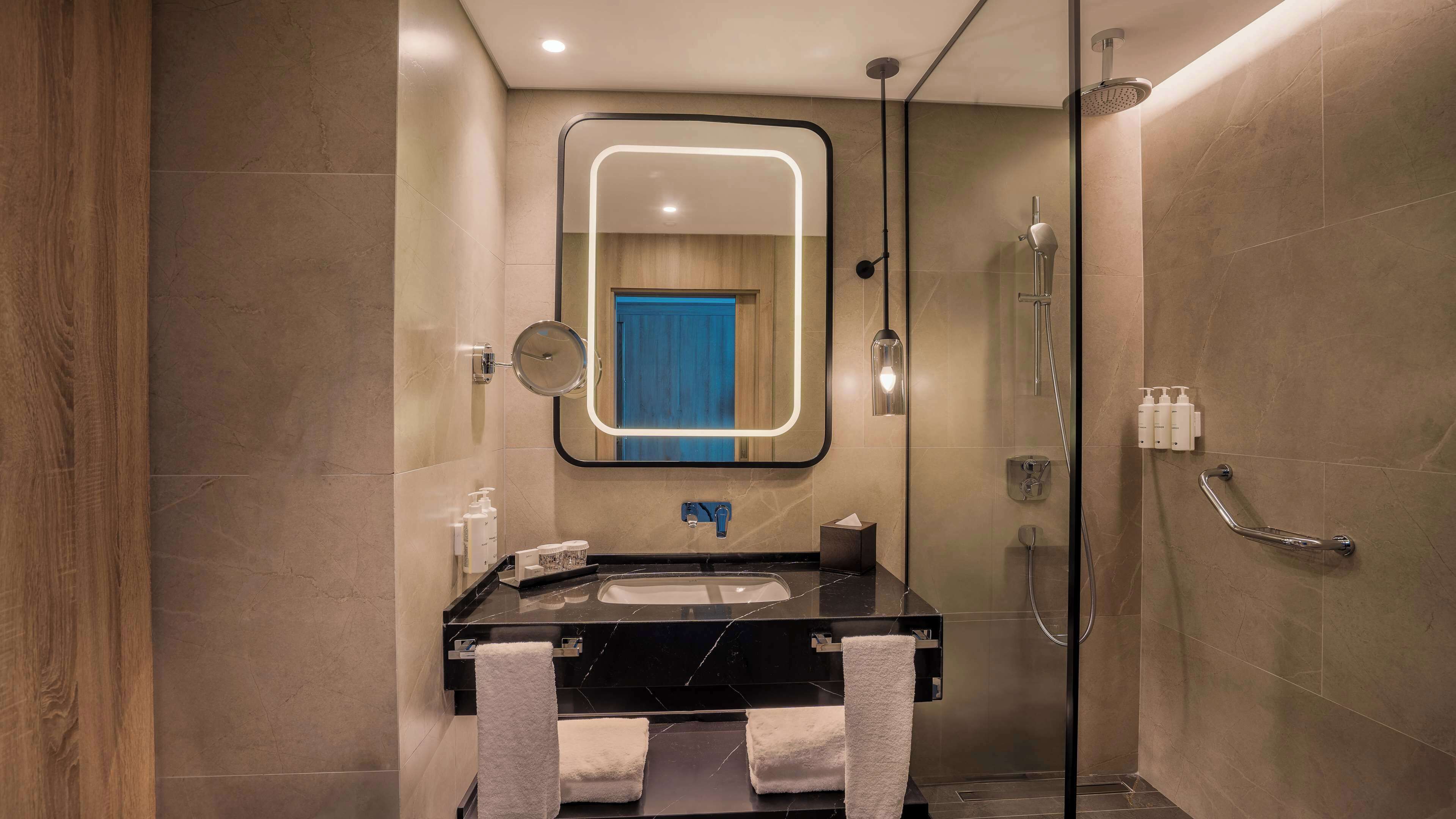 A modern bathroom with a black marble sink, a glass-enclosed shower, and a mirror with a lighted frame.