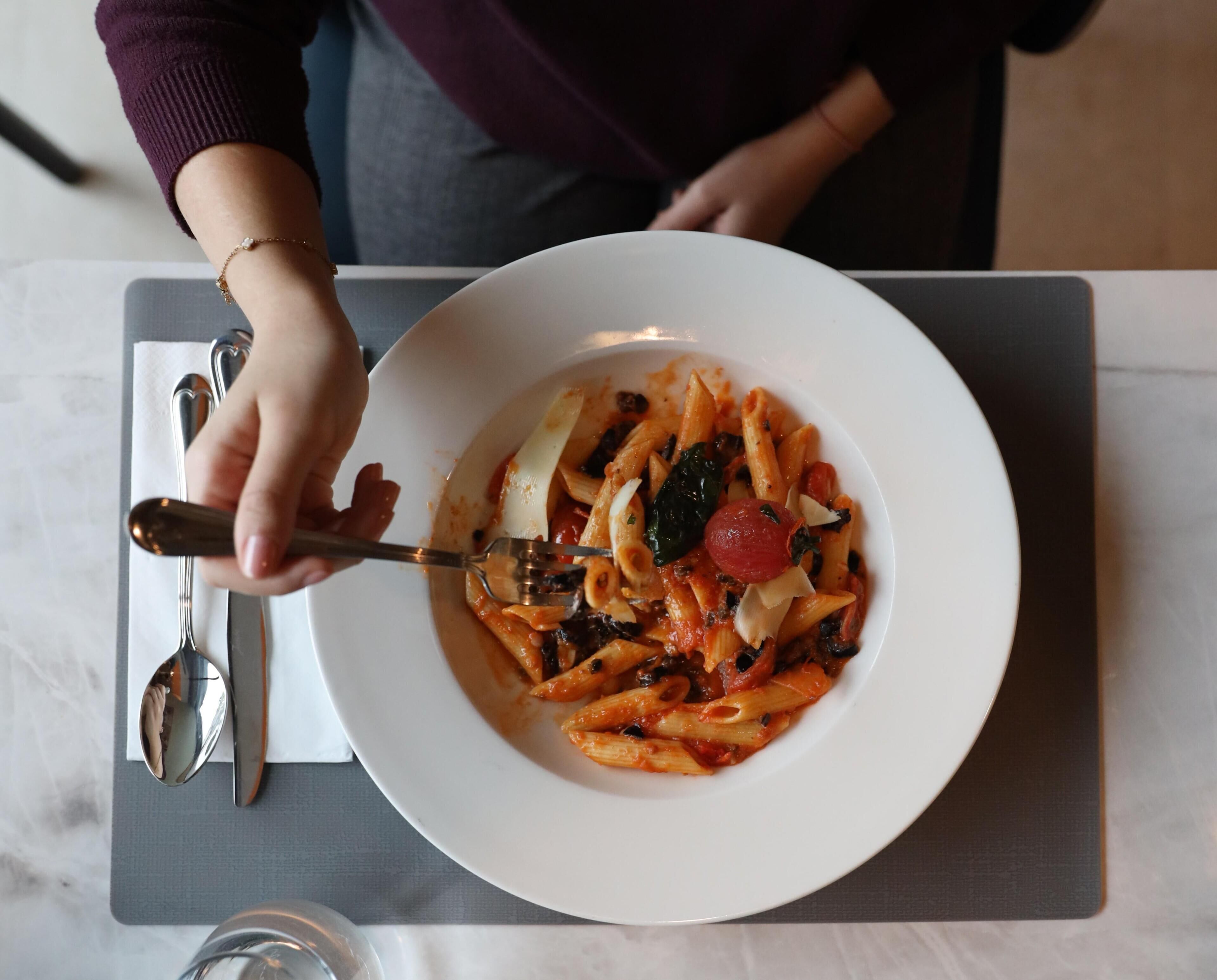 Una persona sirve un plato de pasta en un plato blanco.