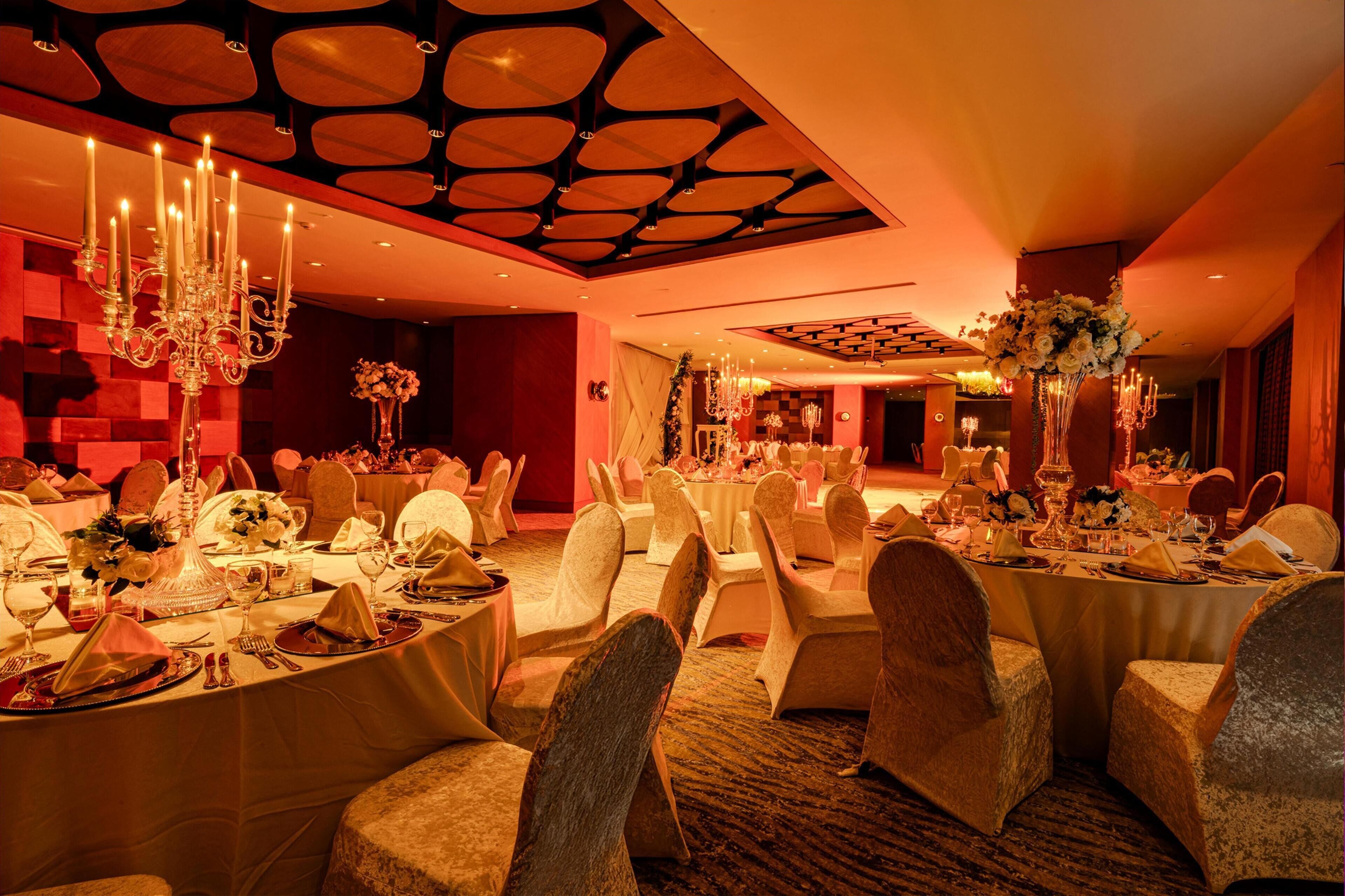 A banquet hall with round tables, white tablecloths, and chairs with white covers.